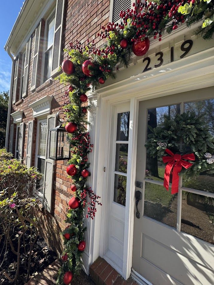 Residential entry with red ornament garland and a bow-trimmed wreath